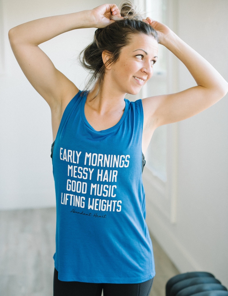 May include: A blue tank top with the text "Early Mornings Messy Hair Good Music Lifting Weights" and the words "Abundant Heart" in smaller font below.