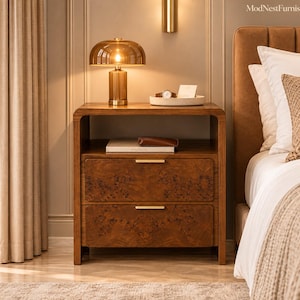 May include: A wooden nightstand with two drawers featuring a burl wood veneer finish and gold-toned horizontal handles. The nightstand has an open top shelf, a brass-colored dome lamp, a white tray with a watch, and a book.