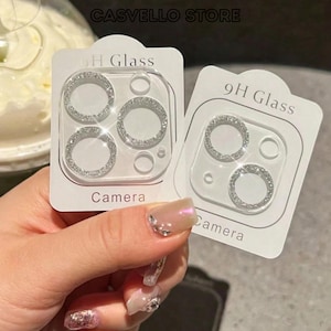 May include: Two white rectangular cards featuring 9H Glass Camera lens protectors. Each card displays circular, silver-toned, rhinestone-encrusted rings designed to fit over smartphone camera lenses, with clear protective glass centres.