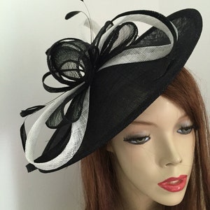 May include: A black and white fascinator hat with a large, curled bow and feathers. The hat is made of a straw-like material and has a wide brim.