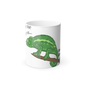 Könnte beinhalten: Ein weißer Keramikbecher mit einer Illustration eines grünen Chamäleons auf einem braunen Ast. Der Text auf dem Becher lautet: 'see me you...' und 'Well, where are you?'. Das Design ist auf der Außenseite des zylindrischen Bechers zentriert.