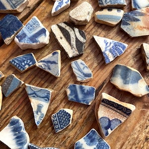 May include: A collection of antique ceramic shards with blue and white patterns, scattered on a wooden surface. The fragments display various designs, including floral and geometric motifs, with visible wear and tear.