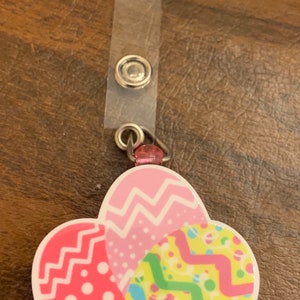 May include: A pink, yellow and blue Easter egg-shaped badge holder with a clear plastic strap and two metal rings.