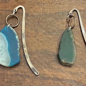 May include: Four unique gemstone bookmarks. Each bookmark features a different colored, teardrop-shaped stone: tan, blue, green, and pink. The stones are attached to silver-colored metal bookmark arms with a small ring.