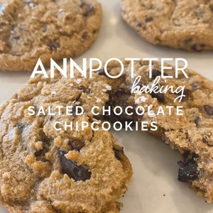 May include: Close-up of a broken chocolate chip cookie with sea salt on top. The cookie is light brown and has a soft, chewy texture. The text "ANNPOTTER baking SALTED CHOCOLATE CHIP COOKIES" is visible in the image.