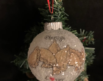 May include: A white, glittery Christmas ornament with a drawing of pierogies and the word "Love" in red.