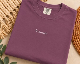 May include: A plum-coloured t-shirt with a crew neckline and short sleeves. The centre of the chest features the white text "it can wait." The interior neck label displays the brand name Comfort Colors and the size L.