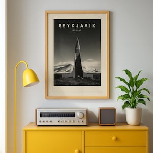 May include: A framed black and white wall art print featuring the Hallgrímskirkja church in Reykjavik, Iceland. The print displays the text REYKJAVIK ICELAND at the top, centred above the tall, pointed architectural structure and snowy mountains.