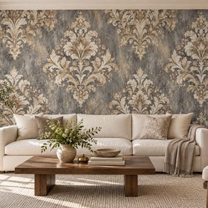 Può includere: Un soggiorno con un grande divano bianco sporco con cuscini decorativi e una coperta, posizionato contro una parete rivestita con carta da parati damascata grigio scuro e beige. Un tavolino in legno si trova davanti con un vaso e libri.