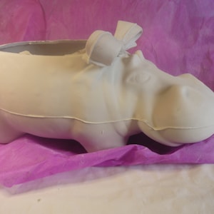 May include: White ceramic hippopotamus planter with a small bow on top. The planter is sitting on a pink tissue paper background.