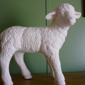 May include: White ceramic lamb figurine with a textured surface, standing on a wooden surface.