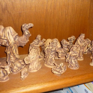 Puede incluir: Un conjunto de figuras de la natividad de cerámica, que incluye un camello, tres reyes magos, un pastor y un bebé Jesús en un pesebre. Las figuras están pintadas en tonos marrones y dorados y tienen un aspecto rústico y vintage.