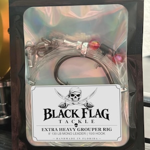 May include: An extra heavy grouper fishing rig in a holographic pouch. The label features a skull with crossed swords and the text: BLACK FLAG TACKLE, EXTRA HEAVY GROUPER RIG, 8' 130 LB MONO LEADER | 10/0 HOOK, HANDMADE IN FLORIDA.