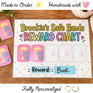 May include: A rectangular reward chart with a white background featuring colorful polka dots. The text reads Brookie's Safe Hands REWARD CHART. It includes two pink rectangular tokens with a sun graphic and the text STAY SAFE, plus three empty spaces with white velcro dots. A blue box at the bottom displays the text Reward: Book.