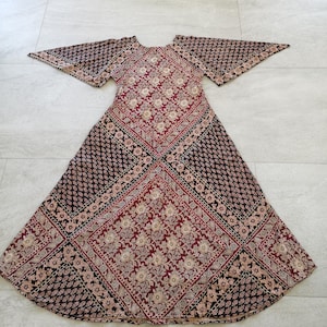 Puede incluir: Un vestido largo y fluido con estampado paisley negro y burdeos. El vestido tiene un escote redondo y mangas acampanadas.