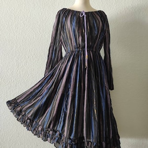 Puede incluir: Un vestido de manga larga a rayas con un dobladillo con volantes. El vestido está hecho de una tela transparente con un brillo metálico. El vestido tiene un lazo en el escote y una cintura ajustada.