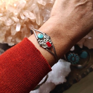 Puede incluir: Un brazalete de plata con un diseño de turquesa y piedra roja. El brazalete está en la muñeca de una persona.