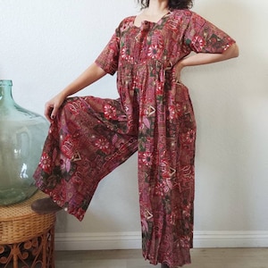 Może przedstawiać: Jednoczęściowy strój w czerwono-zielone wzory z kwadratowym dekoltem i krótkimi rękawami. Komplet ma luźny krój i szerokie nogawki.