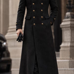May include: A long, charcoal gray double-breasted wool coat featuring a high collar, shoulder epaulets, and two rows of metallic gold buttons. The coat includes flap pockets at the waist, buttoned cuffs, and a full-length hemline.