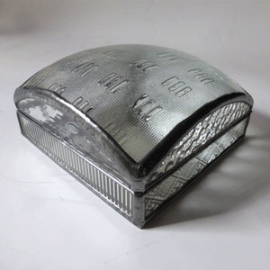 May include: A clear glass box with a silver metal frame. The top of the box is a dome shape with a textured pattern. The bottom of the box has a decorative pattern.