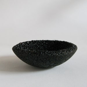 May include: A small, black, ceramic bowl with a textured, bumpy surface.