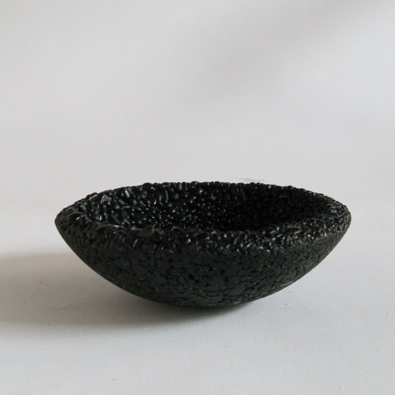 May include: A small, black, ceramic bowl with a textured, bumpy surface.