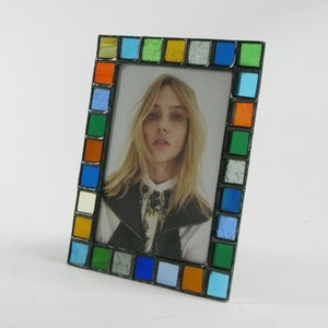 May include: A colorful picture frame with a mosaic of small squares in shades of blue, green, orange, and yellow. The frame is made of metal and has a black finish. A photo of a woman with blonde hair is inside the frame.