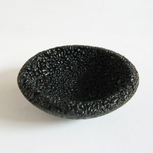 May include: A small, black ceramic bowl with a textured, bumpy surface.