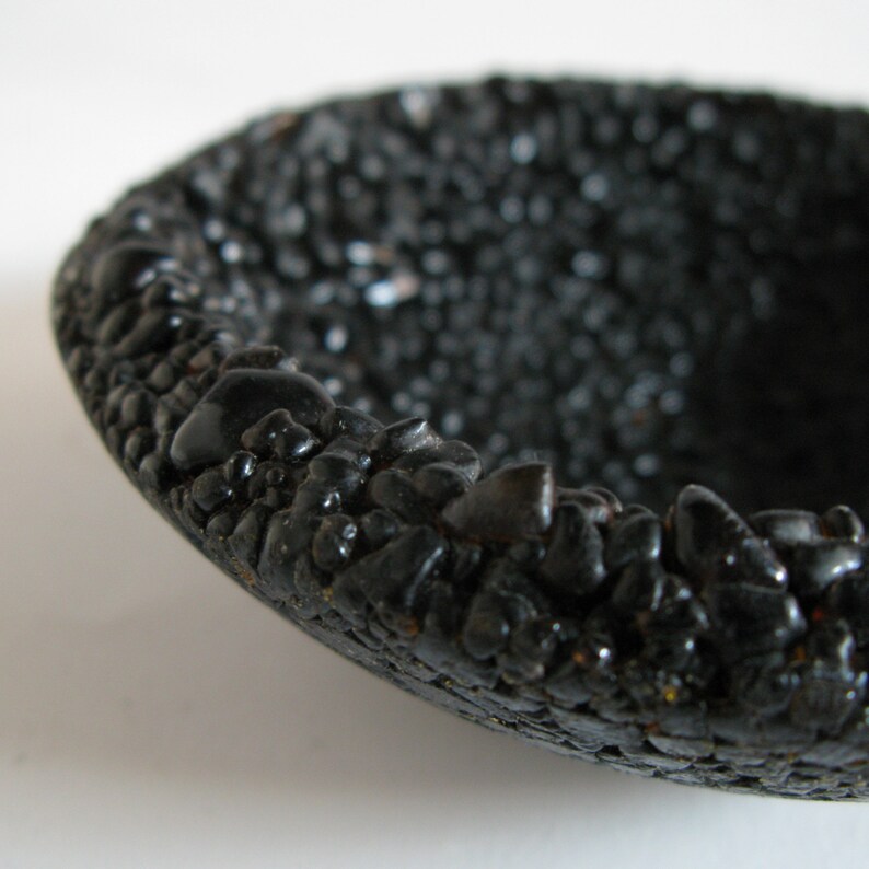 May include: A black bowl made of small black stones. The bowl is round and has a smooth, polished surface.