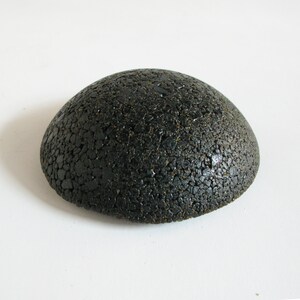May include: A black, round, textured, dome-shaped object. The object is made of small, black, pebble-like pieces.