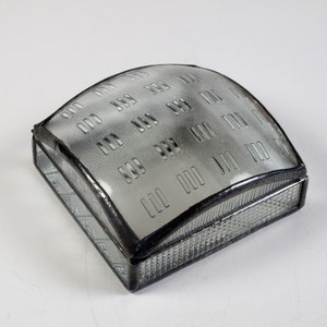 May include: A clear glass box with a patterned lid. The box is made of glass and has a silver metal frame. The lid is curved and has a repeating pattern of small squares.