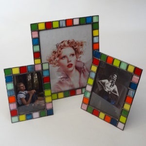 May include: Three colorful picture frames with mosaic tile borders. The frames are different sizes and feature photos of people.