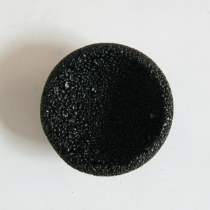 May include: A black, round, textured bowl with a slightly raised rim. The bowl is made of a material that resembles small, black pebbles.