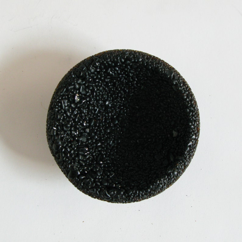 May include: A black, round, textured bowl with a slightly raised rim. The bowl is made of a material that resembles small, black pebbles.