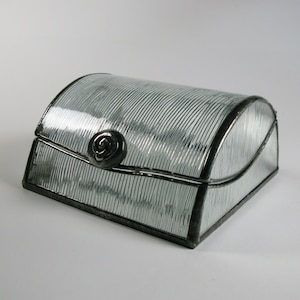 May include: A clear glass box with a silver metal rose design on the lid. The box has a textured, ribbed surface and is made of stained glass.
