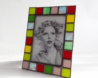 May include: A stained glass picture frame with a colorful mosaic border. The frame is made of small squares of glass in shades of red, yellow, green, and pink. The frame is empty and ready to hold a photo.