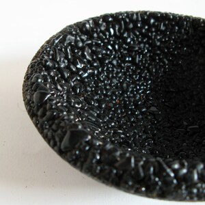 May include: A black bowl with a textured surface that resembles small pebbles. The bowl is made of a smooth, glossy material.