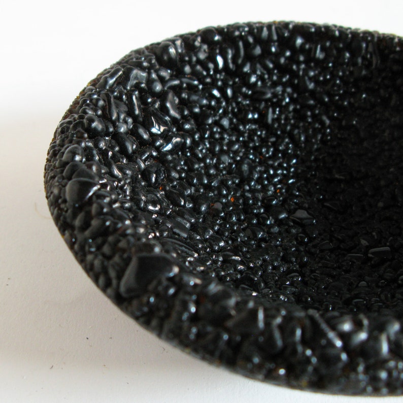 May include: A black bowl with a textured surface that resembles small pebbles. The bowl is made of a smooth, glossy material.