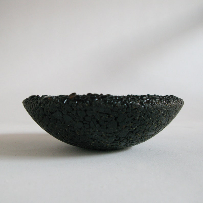 May include: A black ceramic bowl with a rough, textured surface. The bowl is shaped like a half-sphere and has a slightly uneven rim.