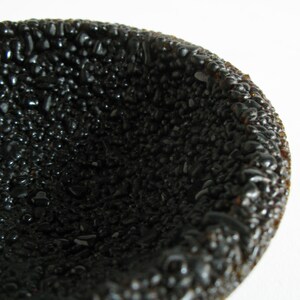 May include: A black bowl made of small, round, textured pieces. The bowl is empty and has a smooth, shiny surface.