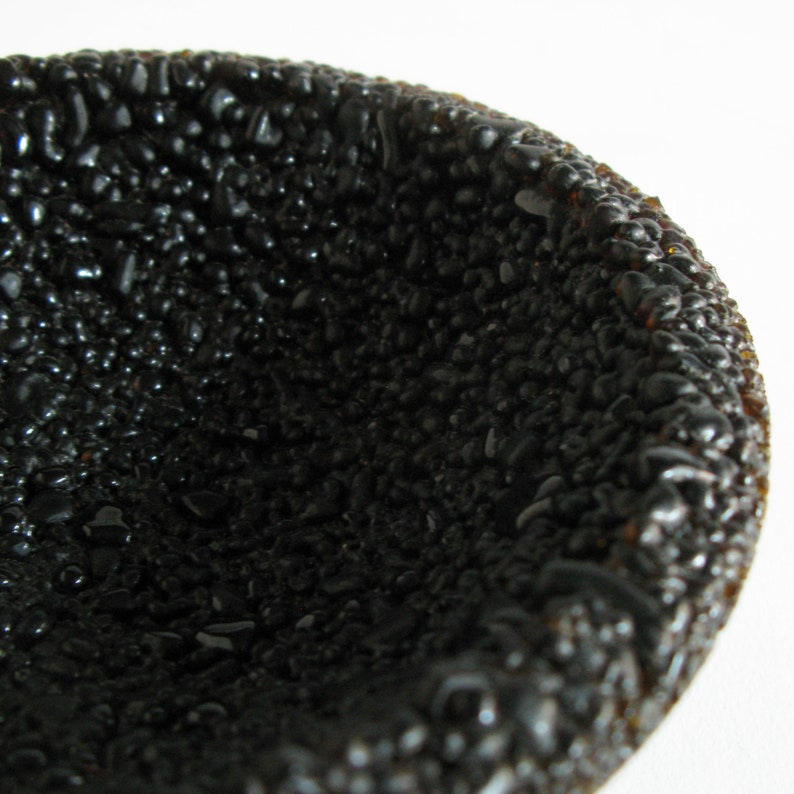 May include: A black bowl made of small, round, textured pieces. The bowl is empty and has a smooth, shiny surface.