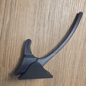 Op de afbeelding: Een zwarte kunststof standaard met een driehoekige voet en een gebogen, langwerpige arm die omhoog steekt. Het object heeft een gladde, matte afwerking en een structureel ontwerp met zichtbare laaglijnen, wat wijst op een 3D-geprinte constructie.