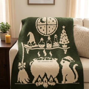 May include: A dark green crochet blanket featuring a cream-coloured design of a moon, stars, a shelf with potion bottles, a witch hat, a Christmas tree, a steaming cauldron over a fire, a broomstick, and a cat wearing a Santa hat.