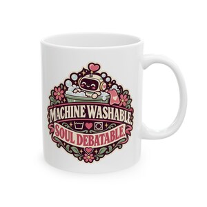 May include: A white ceramic mug featuring a colorful graphic of a small robot in a bubble bath. The text reads "MACHINE WASHABLE" and "SOUL DEBATABLE" with icons of a wash basin, a heart, and a square. The design includes pink flowers and leaves.