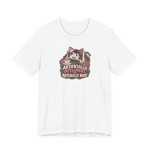 May include: A white short-sleeved t-shirt featuring a central graphic of a cat peeking over a laptop with a teacup and roses. The text reads ARTIFICIALLY INTELLIGENT NATURALLY NOSY in a decorative font with a small heart icon between the words.