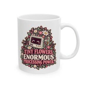 May include: A white ceramic mug featuring a colourful graphic of a smiling vintage computer monitor surrounded by pink and white flowers and green leaves, with the text "TINY FLOWERS, ENORMOUS PROCESSING POWER" printed in pink and cream lettering.