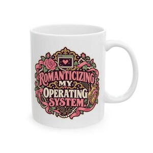 May include: A white ceramic mug featuring a decorative graphic with pink roses, pearls, and ribbons surrounding the text "ROMANTICIZING MY OPERATING SYSTEM" in a stylized font, along with a small computer window icon and a mechanical heart illustration.