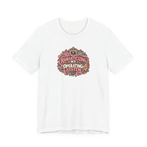 May include: A white short-sleeved t-shirt featuring a central graphic design with the text "ROMANTICIZING MY OPERATING SYSTEM". The illustration includes a pink rose, a heart-shaped anatomical organ, pearls, and ribbons in shades of pink and gold.