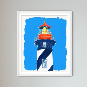 May include: A white framed print of a colorful illustration of a lighthouse against a blue background. The lighthouse is black and white with red and yellow accents. The print is hanging on a wall above a wicker chair.