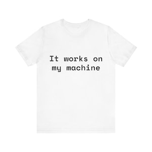 Puede incluir: Una camiseta blanca de manga corta con el texto negro "It works on my machine" impreso en una fuente monoespaciada en el centro del pecho. La prenda tiene cuello redondo, un corte estándar, mangas cortas y un dobladillo recto en la parte inferior.